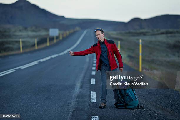 male backpacker hitch hiking on long mountin road - trampen stock-fotos und bilder