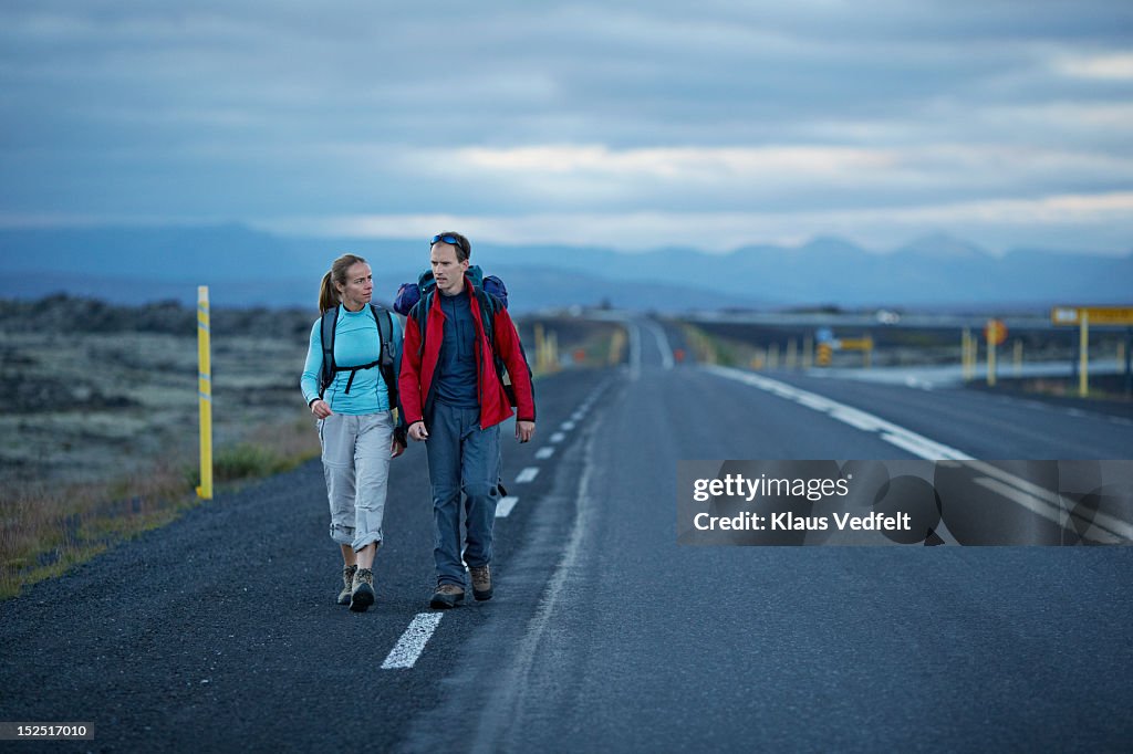 Hiking couple walking alonside long road