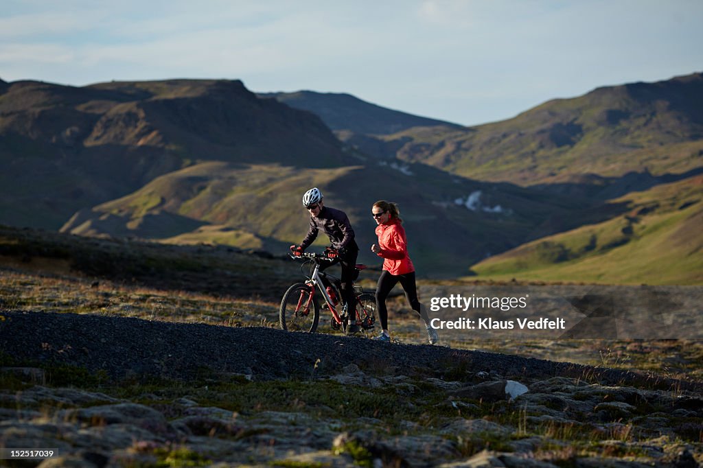 Couple running & biking together on mountain trail