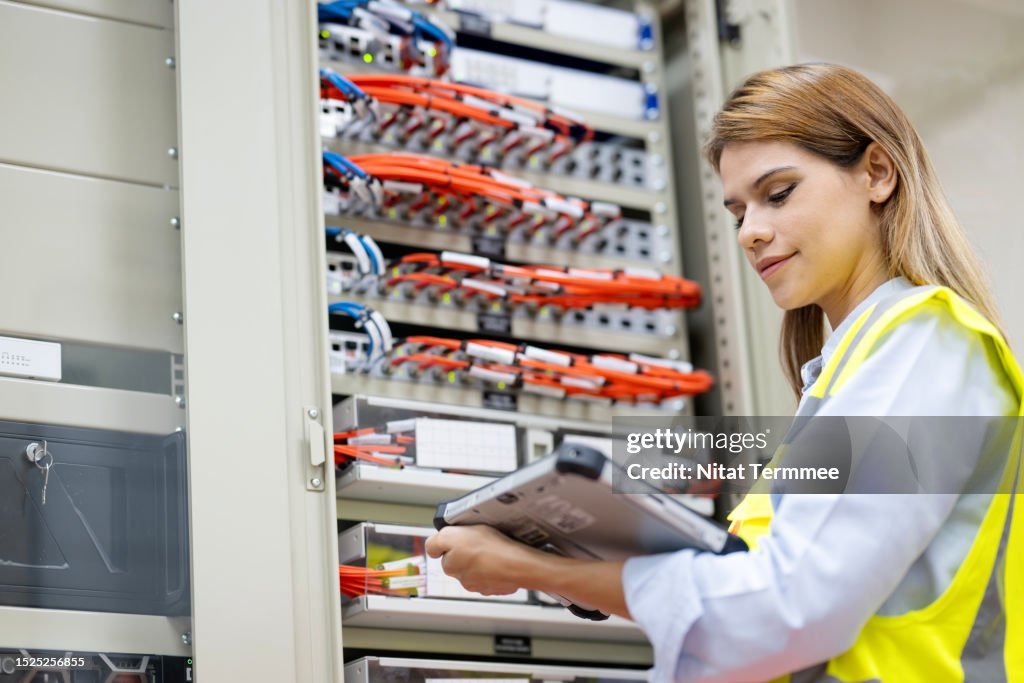 Improved Efficiency and Enhanced Data Protection of Business Operations with Data Center Solutions. A female Network engineer using a tablet computer to troubleshoot and network performance monitoring in a server room.