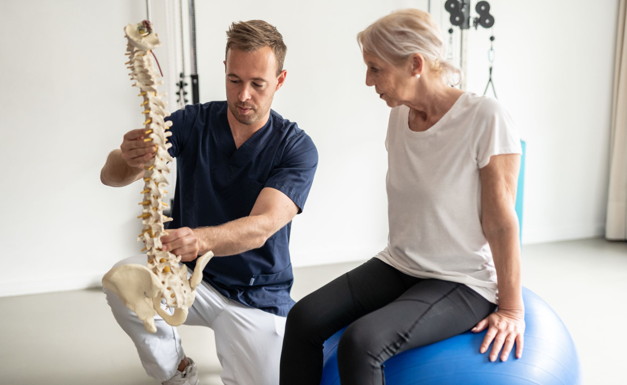 Médico profissional mostrando paciente idoso através de exercícios terapêuticos em uma bola medicinal. Médico profissional mostrando paciente idoso através de exercícios terapêuticos em uma bola medicinal.