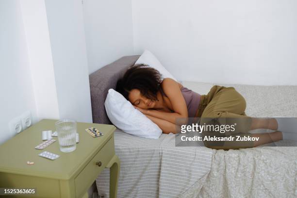 attractive sleeping dark-skinned woman or girl in the bedroom. a glass of water, pills, medicines and medicines on the bedside table next to the bed. the concept of lack of sleep, fatigue, lack of melatonin. treatment and prevention of insomnia. - hormoon stockfoto's en -beelden