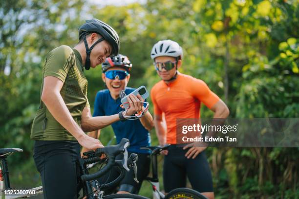 asian chinese male professional cyclist resting in rural scene, showing smartphone mobile app gps coordinates to his team . travel, sport and modern technology concept. - cyclist stock pictures, royalty-free photos & images