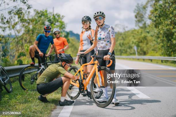 asian chinese cyclist helping his team checking on bicycle chain at roadside in rural scene weekend morning - triathlon gear stock pictures, royalty-free photos & images