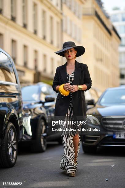 Merve Gorgotz wears a black braided wicker large hat, gold large cut-out FF logo pendant earrings, a black and white zebra print pattern V-neck /...