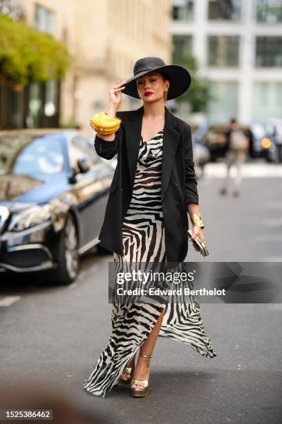 Merve Gorgotz wears a black braided wicker large hat, gold large cut-out FF logo pendant earrings, a black and white zebra print pattern V-neck /...