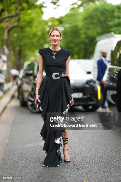 Helena Bordon wears silver black earrings, black sunglasses, a black shoulder-pads / sleeveless / long asymmetric slit dress with silver embroidered...