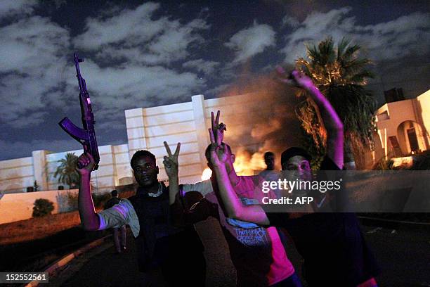 Libyan demonstrator holds up a gun as others flash the victory sign and a car burns in the background near the headquarters of the hardline Islamist...
