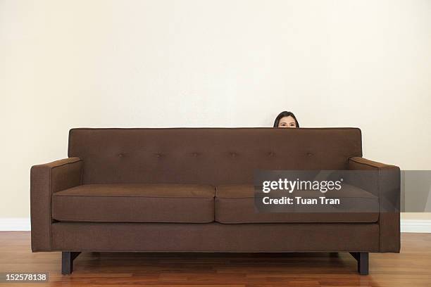 woman hiding behind sofa - una mujer de mediana edad solamente fotografías e imágenes de stock