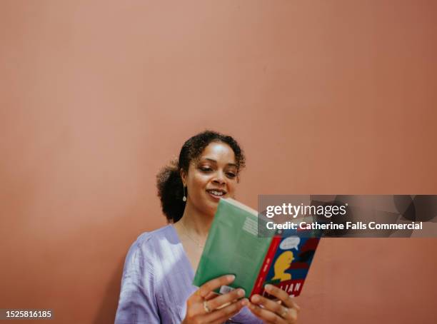 a woman reads a book against a plain background, with space for copy. - processo de tradução imagens e fotografias de stock