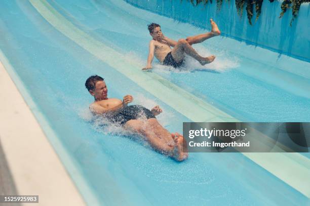 teenage boys having fun sliding in a waterpark - water slide stock pictures, royalty-free photos & images