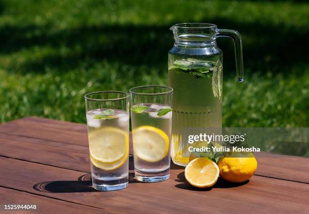 lemonade in glass jug on wooden table outdoors. summer refreshing drink. cold detox water with lemon - lemon soda stock pictures, royalty-free photos & images
