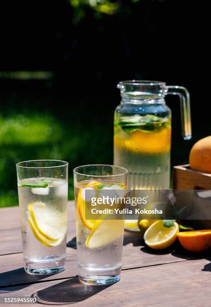 lemonade in glass jug on wooden table outdoors. summer refreshing drink. cold detox water with lemon - crushed leaves stock pictures, royalty-free photos & images