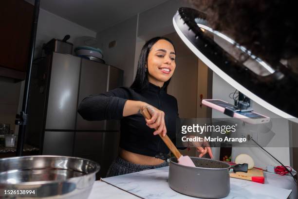 latin woman youtuber is in the kitchen of her house with the help of her assistant, she records a video of recipes for her youtube followers - social content stock pictures, royalty-free photos & images