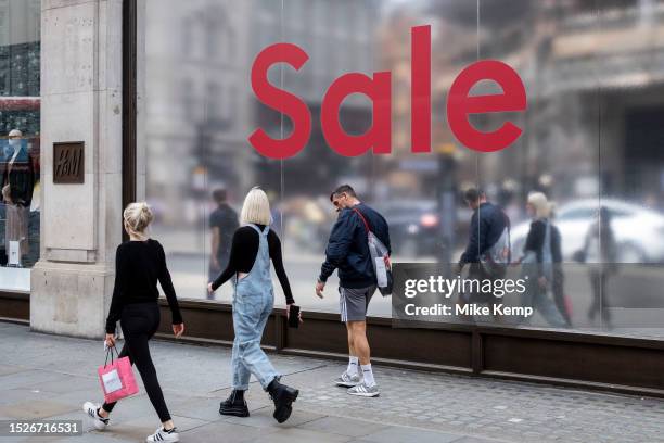 People out shopping walk past a large scale sale sign in red and silver for major high street clothing brand H&M outside their flagship store on the...