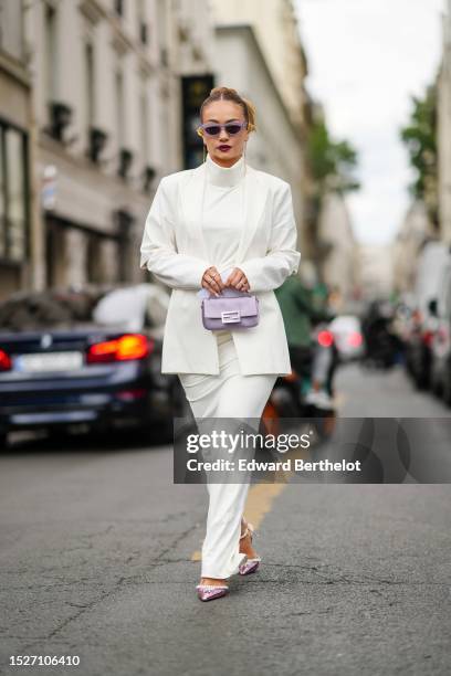 Merve Gorgotz wears pale purple sunglasses, a white turtleneck sleeveless / cut-out waist / wide legs jumpsuit, a white blazer jacket, a pale purple...