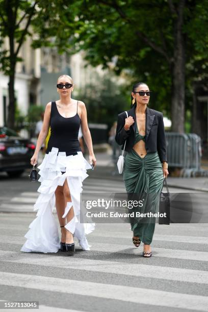 Justyna Czerniak wears black sunglasses, gold ball earrings, a black asymmetric shoulder straps body, a white embroidered large fringed squared slit...