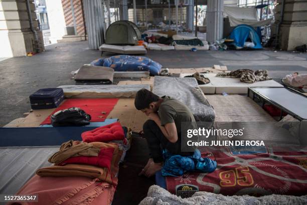 Man on his mattress looks at his phone in the migrant camp in the Stalingrad district of Paris on July 12, 2023.