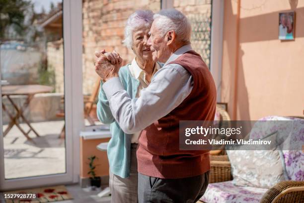 una pareja de pelo plateado bailando en su salón durante el aislamiento - plano fijo fotografías e imágenes de stock