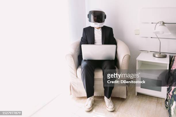man wearing suit jacket and astronaut helmet, sitting in an armchair in a bedroom with a bay window, working with a laptop. concept of explorer, scientist, weirdness, space exploration, creativity. - superman reveal stock pictures, royalty-free photos & images