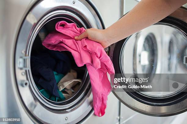 woman putting shirt into washing machine - washing machine stock-fotos und bilder