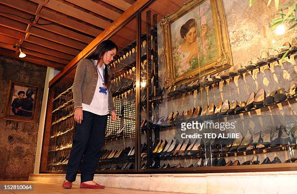 Museum employee checks shoes of former Philippine first lady Imelda Marcos, next to her portraits displayed at the shoe museum in Manila on September...