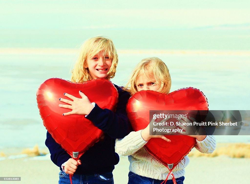 Two girls holding red heart balloons