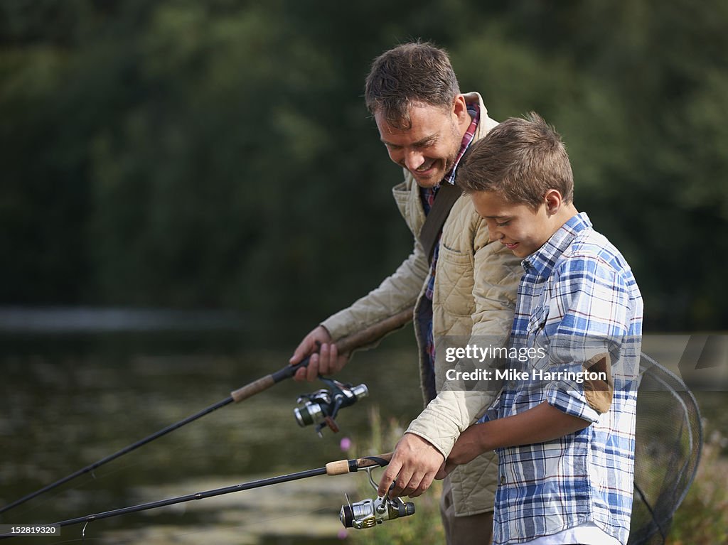 Father assisting son with fishing rod.