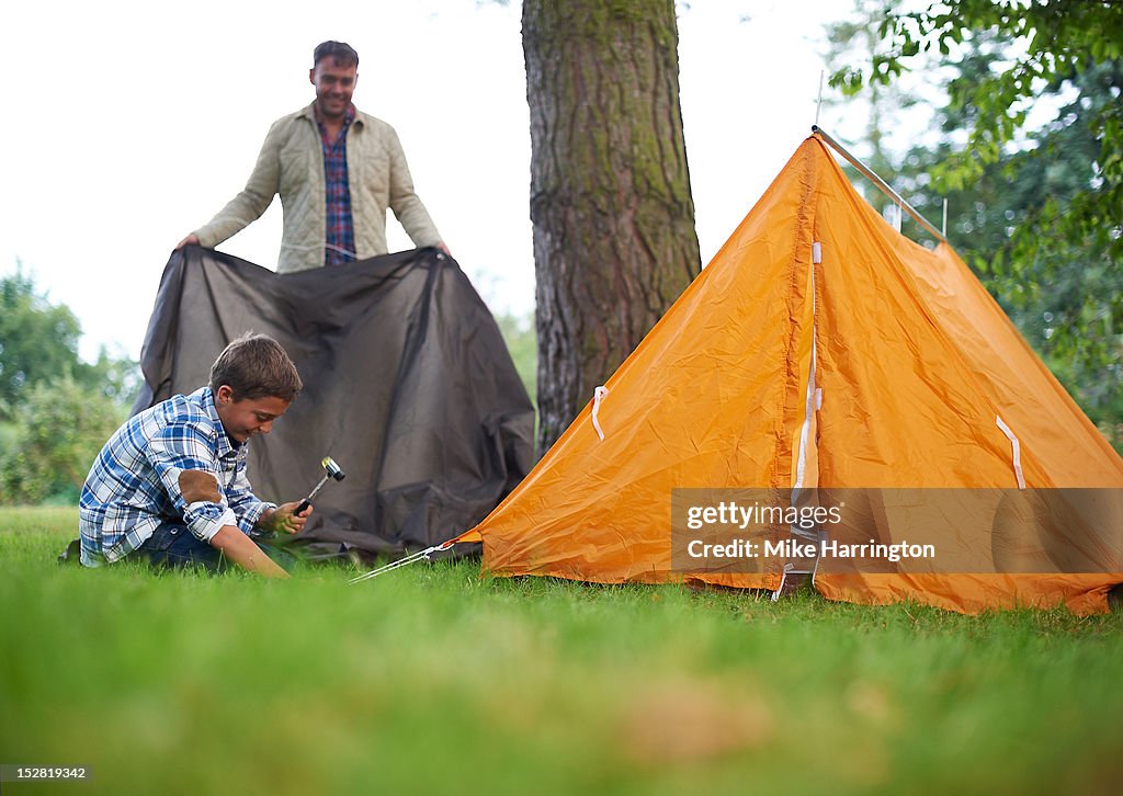 Father and son pitching tent in rural location.