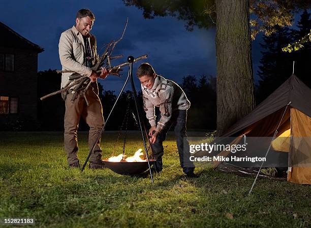 father and son fuelling fire outside tent. - brasero photos et images de collection