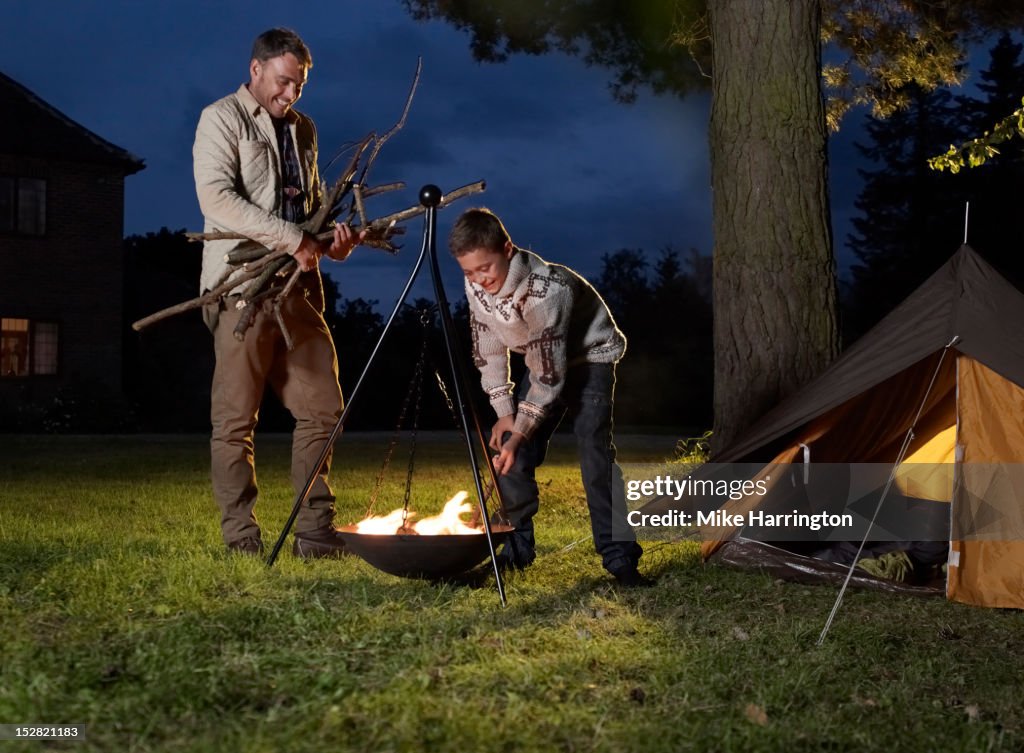 Father and son fuelling fire outside tent.