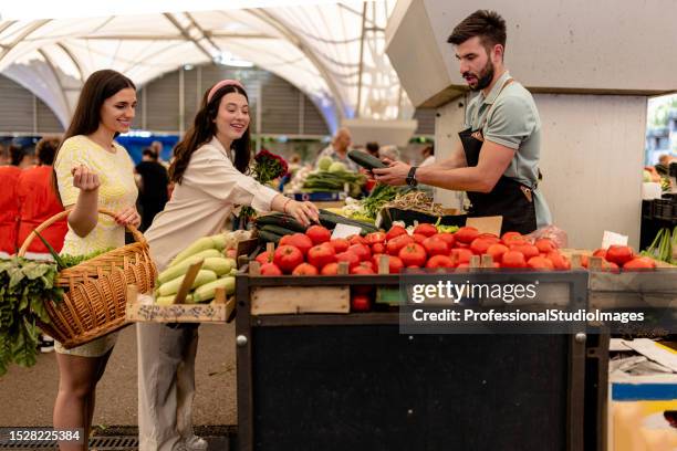 deux femmes découvrent les meilleurs légumes offerts par un vendeur réputé au marché de rue - homegrown produce stock photos et images de collection