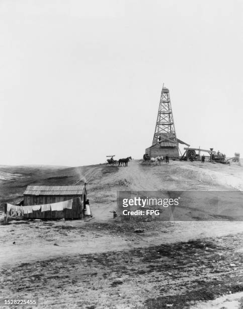 People and horse-drawn carriages before a lone derrick at a Century Oil Company drilling operation in the Kern River District of California, circa...