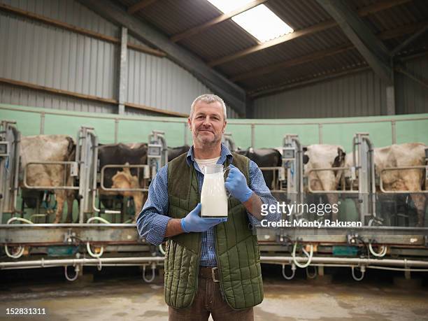 portrait of farmer holding jug of milk in rotary milking parlour on dairy farm with cows - leiteiro - fotografias e filmes do acervo