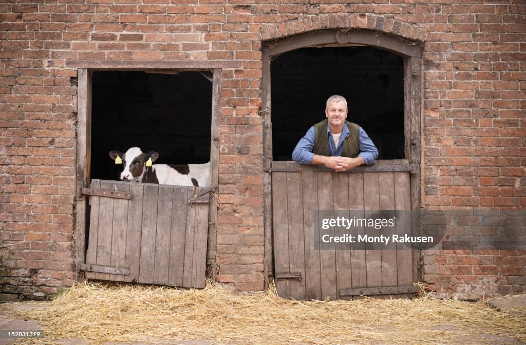 Portrait of farmer leaning on stable door with calf