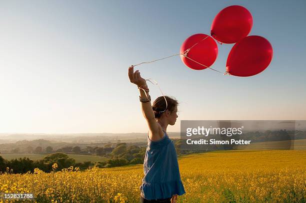 girl carrying balloons in field - balloon girl stock pictures, royalty-free photos & images