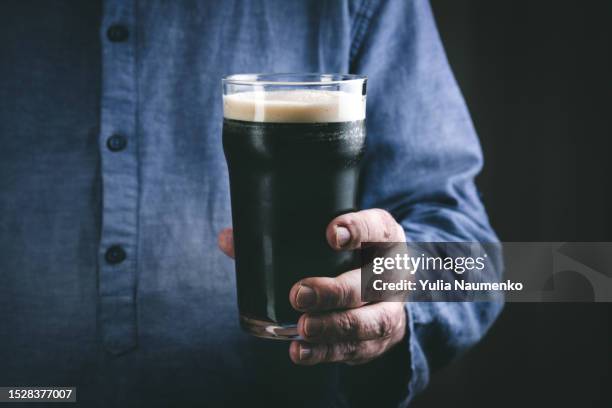 a glass of dark beer in the hands of an elderly man. - craft beer stock pictures, royalty-free photos & images