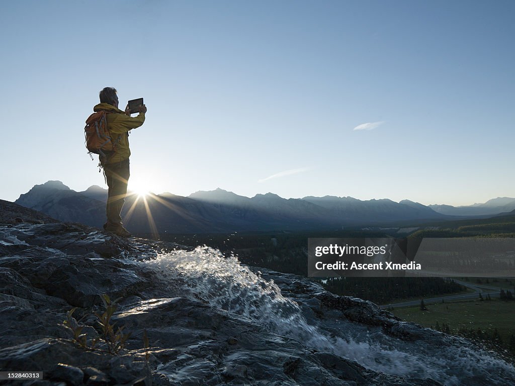 Man takes picture of sunrise over mountains