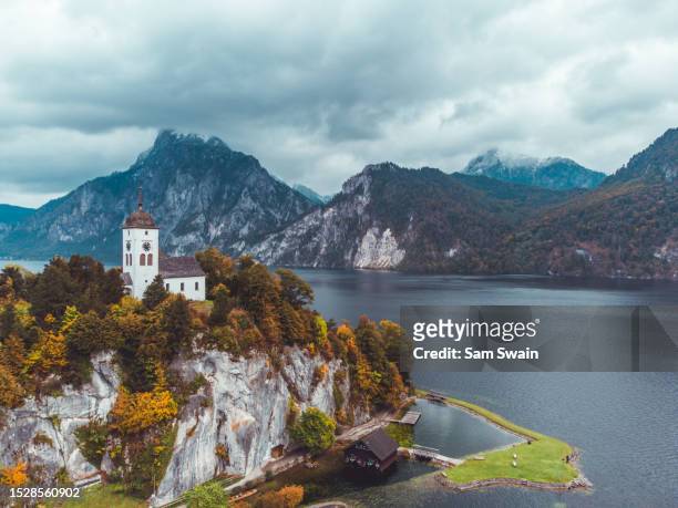 drone shot of a church on the traunsee lake with traunstein mountain in the back ground during autumn in austria. - gmunden austria stock pictures, royalty-free photos & images