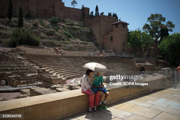 Tourists are seen sitting and holding an umbrella to protect themselves from the sun as they rest in downtown city amid an intense heatwave in...