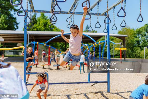 girl swinging on jungle gym at school recess - speeltuintoestellen stockfoto's en -beelden