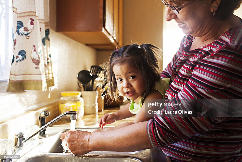 Woman washes toddler hands at kitchen sink