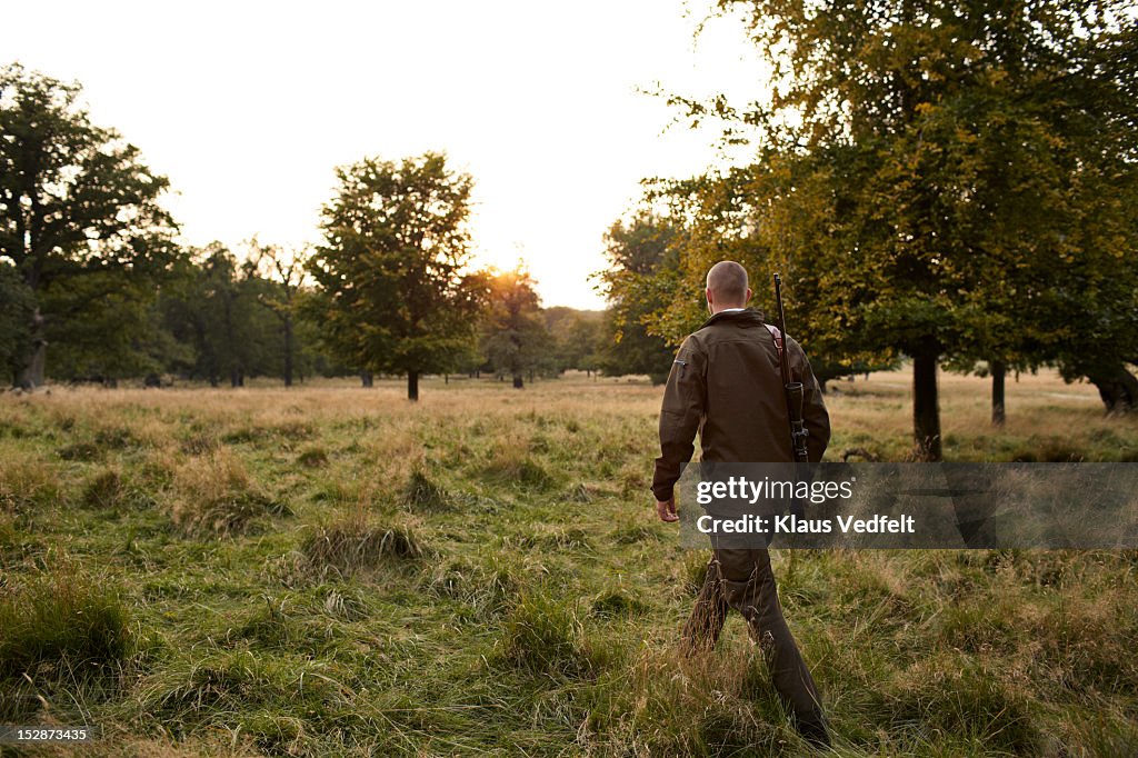 Male hunter walking towards sunset on grassfield