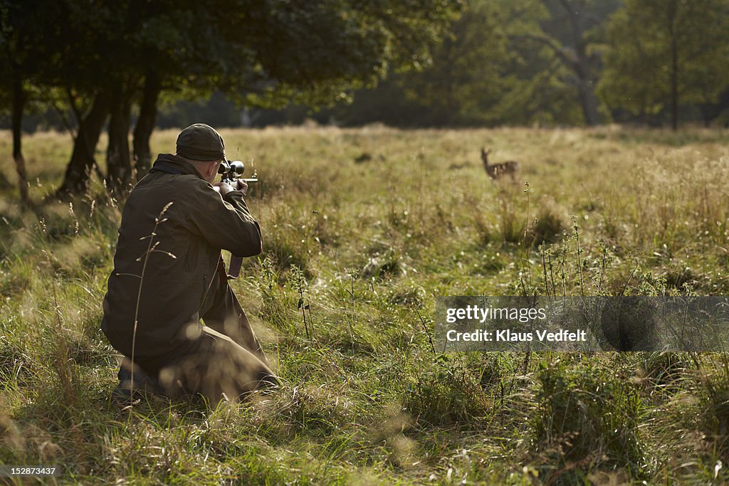 Male hunter aiming at deer with rifle