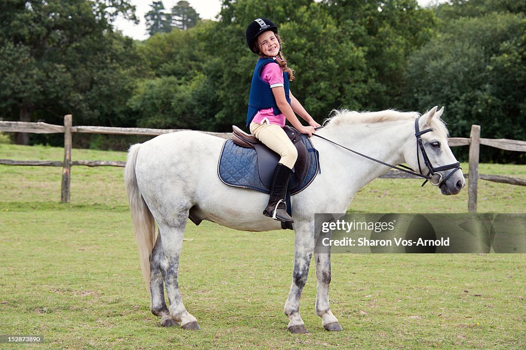 Girl with beaming smile riding grey pony
