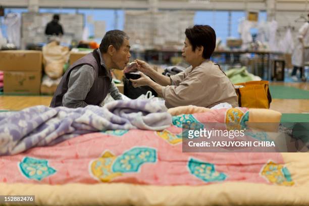 Shizuko Abe helps her paralysed 73-year-old husband Yoshio eat at an evacuation centre for hospital patients displaced by the earthquake and tsunami,...
