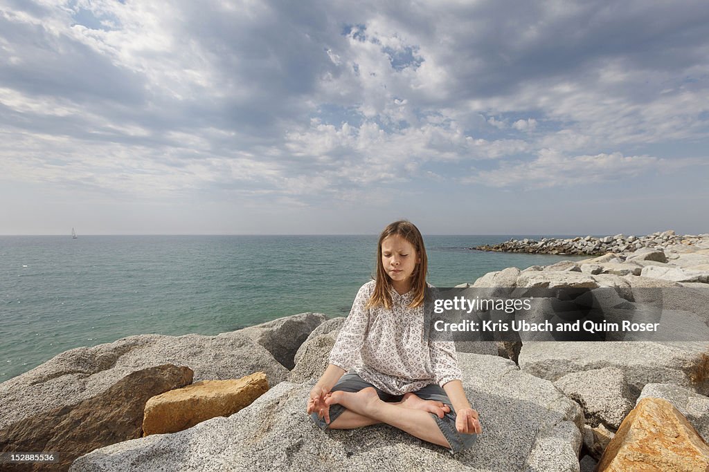 Girl meditating on rocks at beach