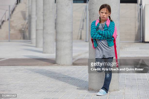 frowning girl leaning against column - kids standing crossed arms stock-fotos und bilder