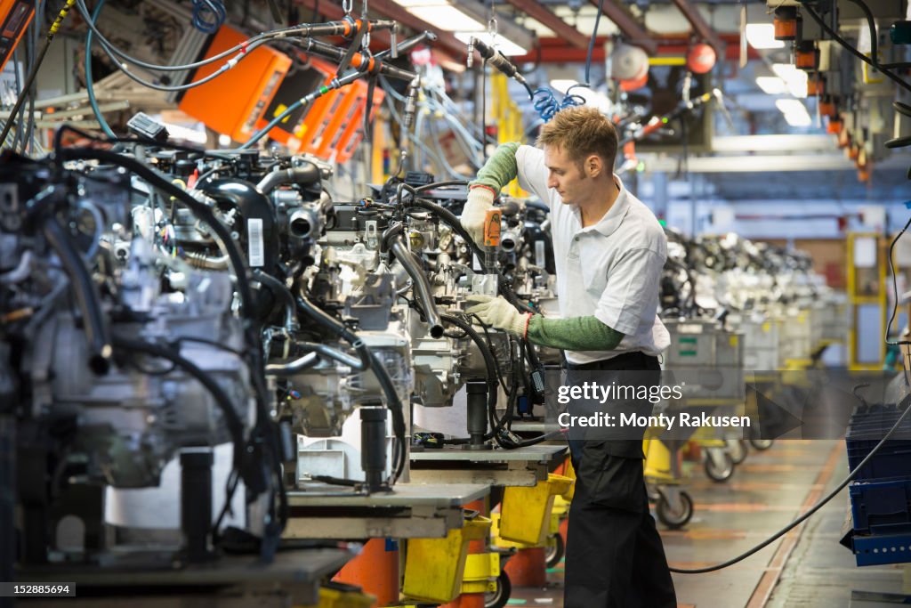 Worker with engines on production line in car factory