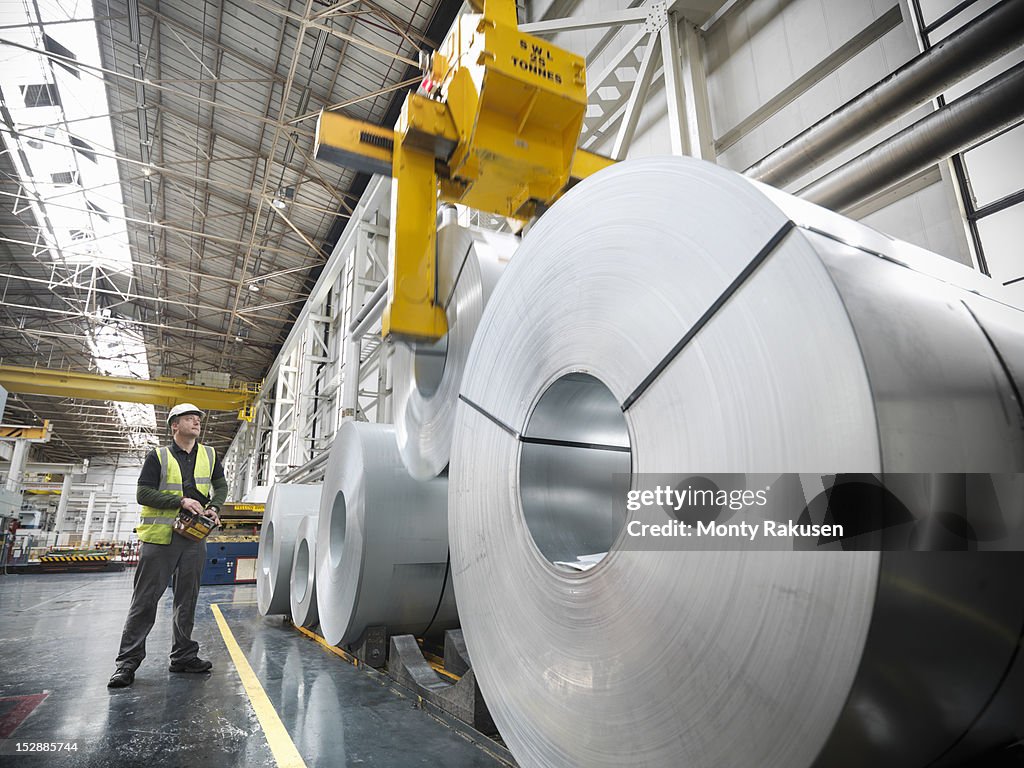 Worker operating crane with steel rolls in car factory